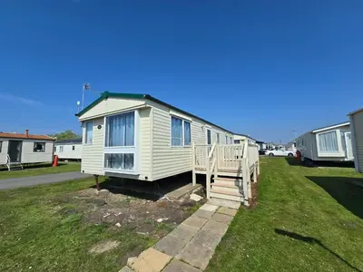 a small white house with a porch on the grass at FI005 Loomy Escapes Caravan at St Osyth Beach Essex in Saint Osyth