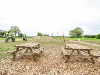 two picnic tables and a playground in a field at Woodpecker in Cambridge