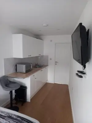 a small white kitchen with a desk and a television at The Southend Airport Lodge in Southend-on-Sea