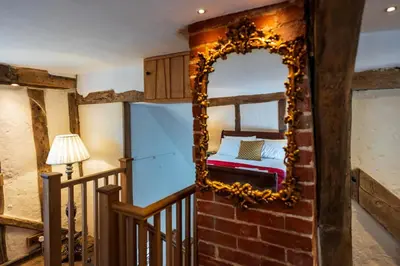 a bedroom with a mirror on a brick wall at Taper House - Cosy Medieval Cottage in Kersey