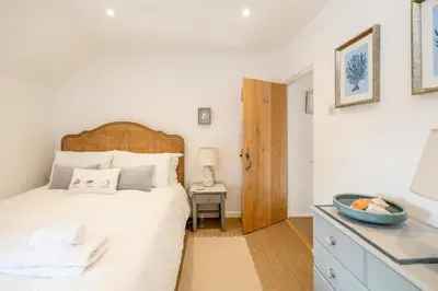 a white bedroom with a bed and a table at Seahorse Cottage, Aldeburgh - sleeps 4 - Adult only property - Managed by Aldeburgh Coastal Cottages in Aldeburgh