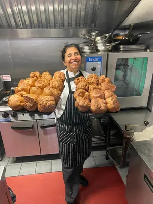 a woman in a kitchen holding a tray of muffins at Thomas Paine Hotel in Thetford