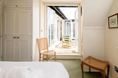 a bedroom with a bed and a balcony with chairs at Claysmead - A large Lakeside House in Thorpeness - Aldeburgh Coastal Cottages in Thorpeness