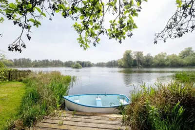 a boat on a dock on a lake at Claysmead - A large Lakeside House in Thorpeness - Aldeburgh Coastal Cottages in Thorpeness