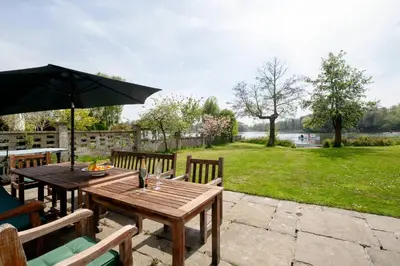 a wooden table and chairs with an umbrella at Claysmead - A large Lakeside House in Thorpeness - Aldeburgh Coastal Cottages in Thorpeness