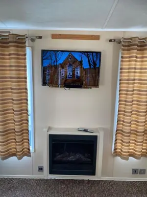 a living room with a fireplace and two windows at Hadleigh Caravans at Seawick Clacton in Clacton-on-Sea