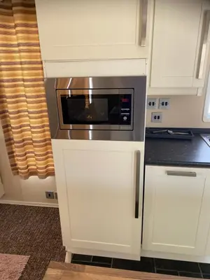 a kitchen with white cabinets and a microwave at Hadleigh Caravans at Seawick Clacton in Clacton-on-Sea