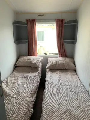 two beds in a small room with a window at Seawick holiday park caravan in Saint Osyth