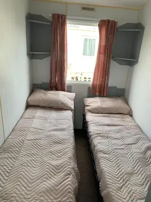 two beds in a small room with a window at Seawick holiday park caravan in Saint Osyth