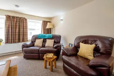 a living room with a leather couch and a chair at Pebbles, King St - Aldeburgh Coastal Cottages in Aldeburgh