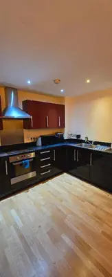 a kitchen with black cabinets and a wooden floor at 1 bed luxurious flat in Basildon