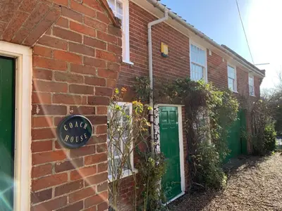 a brick building with a green door and a sign at The Coach House, Framsden