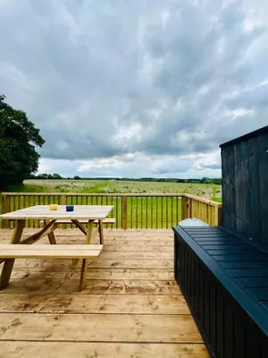 a wooden deck with a picnic table and a fence at Unique Suffolk Cabin with Countryside Views in Burgh