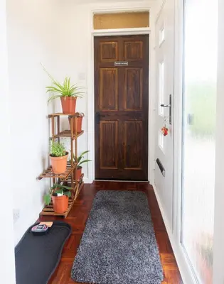 a hallway with a wooden door with plants and a rug at Lazy Acre, Suffolk in Hopton