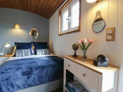 a bedroom with a bed with blue sheets and a window at Luxury Shepherd Hut with Private Hot Tub in Swaffham Bulbeck
