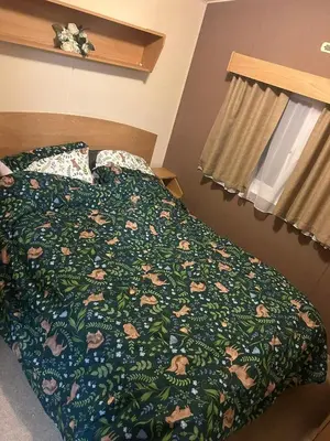 a bedroom with a bed with a green comforter at 2 bed caravan seawick hoilday Park in Clacton-on-Sea