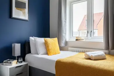 a bedroom with blue walls and a bed with a yellow blanket at Beaulieu Rest 3 Bed House Chelmsford in Broomfield