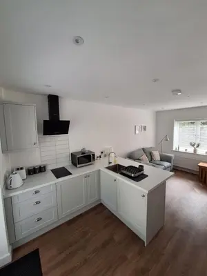 a kitchen with white cabinets and a living room at New Annexe in Gosfied in Gosfield