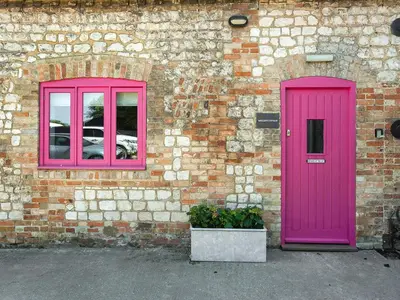 a brick building with a pink door and windows at Moglett Cottage in Fincham