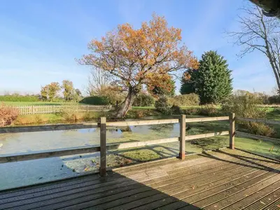 a wooden boardwalk with a fence next to a pond at Pond View Cottage - Uk48230 in Tibenham
