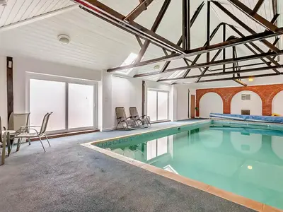 a large swimming pool in a room with a table and chairs at The Retreat - Uk48231 in Tibenham