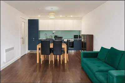 a living room with a green couch and a table and chairs at Modern 2 Bed Flat with parking Next to Basildon Station in Laindon