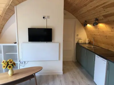 a kitchen with a table and a tv on the wall at Muntjac Cabin in Elmswell