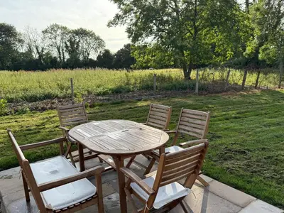 a wooden table and chairs on a patio with a field at The Den in Scoulton