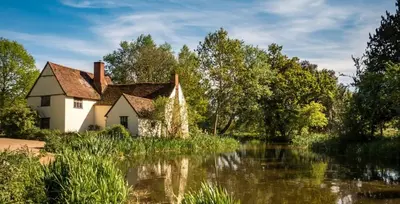 an old house next to a river with trees at The Sun Inn in Dedham