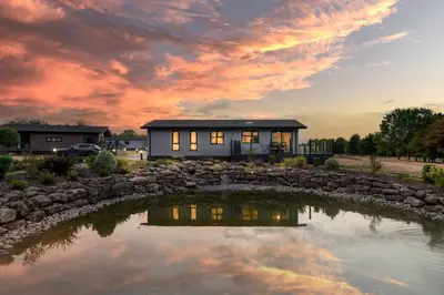 a house with a pond in front of it at Finest Retreats - Cambridge Luxury Lodge