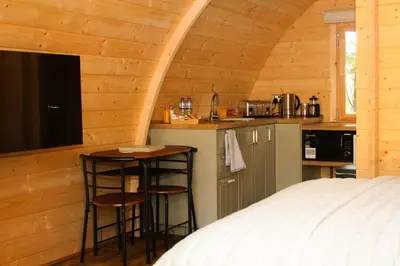 a bedroom with a bed and a kitchen with stools at Highgate Cabin in Takeley