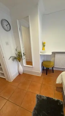 a room with a clock on the wall and a vase with flowers at Peaceful Springfield Studio in Chelmsford