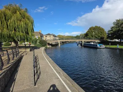 a person sitting on a bench next to a river at Stunning One Bed Flat at Dawe Luxury Suites - An Entire Apartment near Ely Cathedral & Train Station - The Perfect Base to Explore Ely, Cambridge, Norfolk & London - 2 Guests Max in Ely