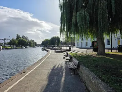 a row of park benches next to a river at Stunning One Bed Flat at Dawe Luxury Suites - An Entire Apartment near Ely Cathedral & Train Station - The Perfect Base to Explore Ely, Cambridge, Norfolk & London - 2 Guests Max in Ely