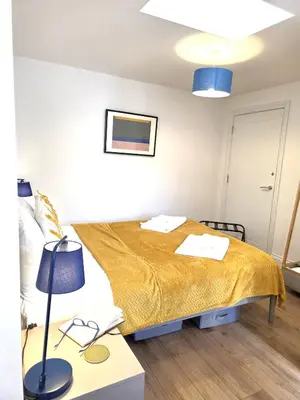 a bedroom with a bed and a table with a lamp at Modern One Bed Flat at Dawe Luxury Suites - An Entire Apartment near Ely Cathedral & Train Station - The Perfect Gateway to Explore Ely, Cambridge, Norfolk & London - Sleeps up to 4 in Ely