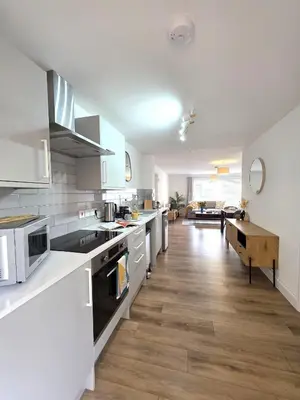 a kitchen with white cabinets and a wooden floor at Modern One Bed Flat at Dawe Luxury Suites - An Entire Apartment near Ely Cathedral & Train Station - The Perfect Gateway to Explore Ely, Cambridge, Norfolk & London - Sleeps up to 4 in Ely