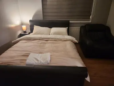 a large bed in a room with a chair at Stacey's Cozy Home in Basildon