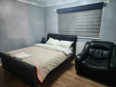 a bedroom with a bed and a leather chair at Stacey's Cozy Home in Basildon