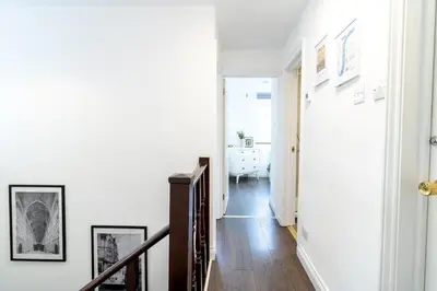 a hallway with white walls and a staircase with wood floors at Large 6-BDR House in Cambridge in Barnwell Junction Station