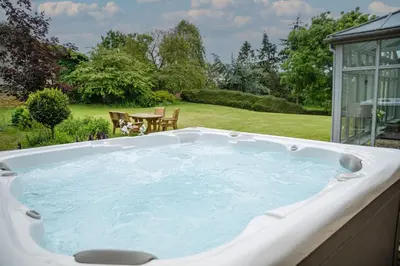 a jacuzzi tub in a garden with a table at Holbecks House by Group Retreats in Hadleigh