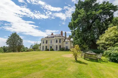 a large house on a grassy field with a bench at Holbecks House by Group Retreats in Hadleigh