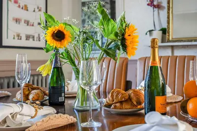 a table with flowers and bottles of wine and bread at 6 Bedroom - Luxury - Cinema Room in Hertford
