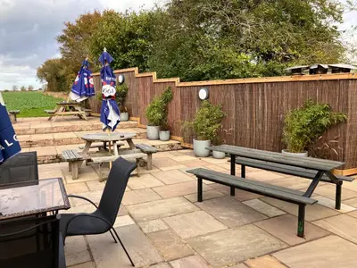 a patio with benches and tables and a fence at White hart public house in Ashill