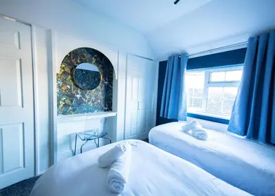 a bedroom with two beds with blue curtains and a window at Bright & Airy 4x Bed House with Parking in Ely