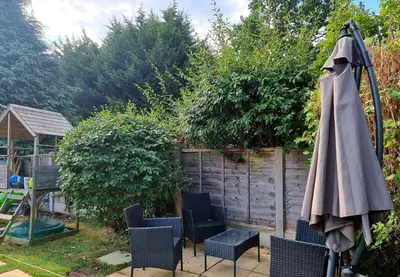 a patio with an umbrella and chairs and a fence at 3-bedroom family home with large garden and free parking in Loughton