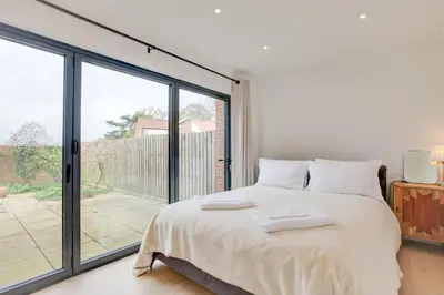 a white bedroom with a bed and a large window at Two bedroom house with far-reaching country views in Sheering