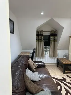 a brown leather couch in a living room with a window at A Cosy and Spacious Studio Flat in Navestock