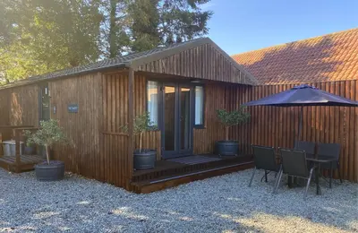 a wooden cabin with a table and chairs and an umbrella at Woodstock Park The Tawny Lodge in Wereham