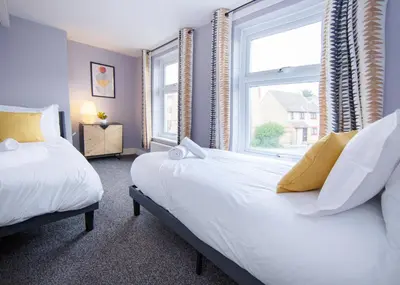 two beds in a room with two windows at Stylish central location 3 bedroom house in Ely