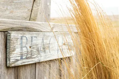 a wooden sign on a wooden fence with tall grass at Chicoutimi 4 in Thorpeness